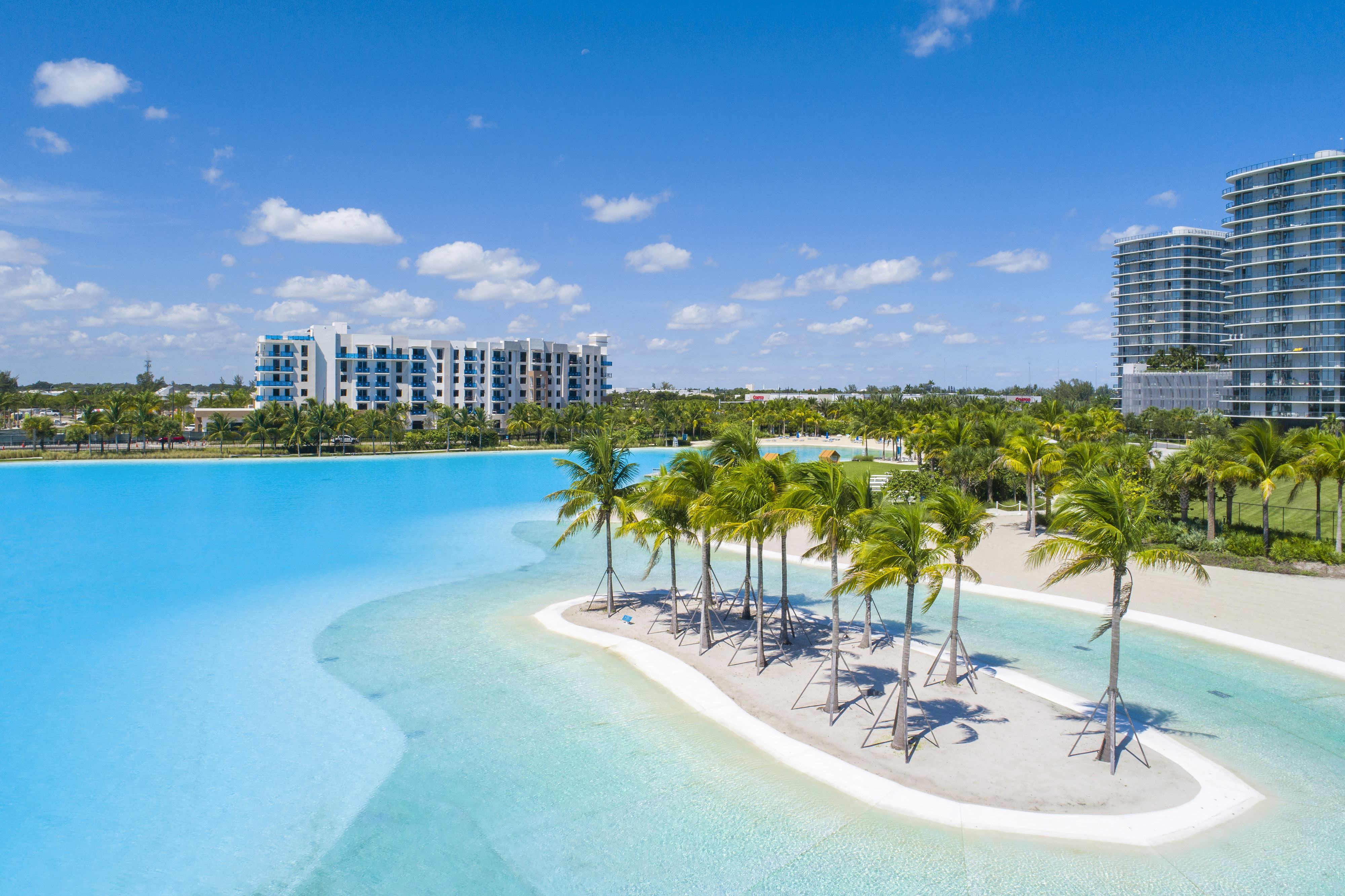 A large swimming pool surrounded by palm trees and a sandy area.